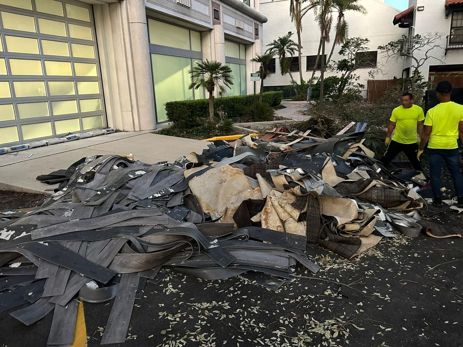 Crew in hi-vis staging torn carpet and stripped roofing outside a storm-hit building