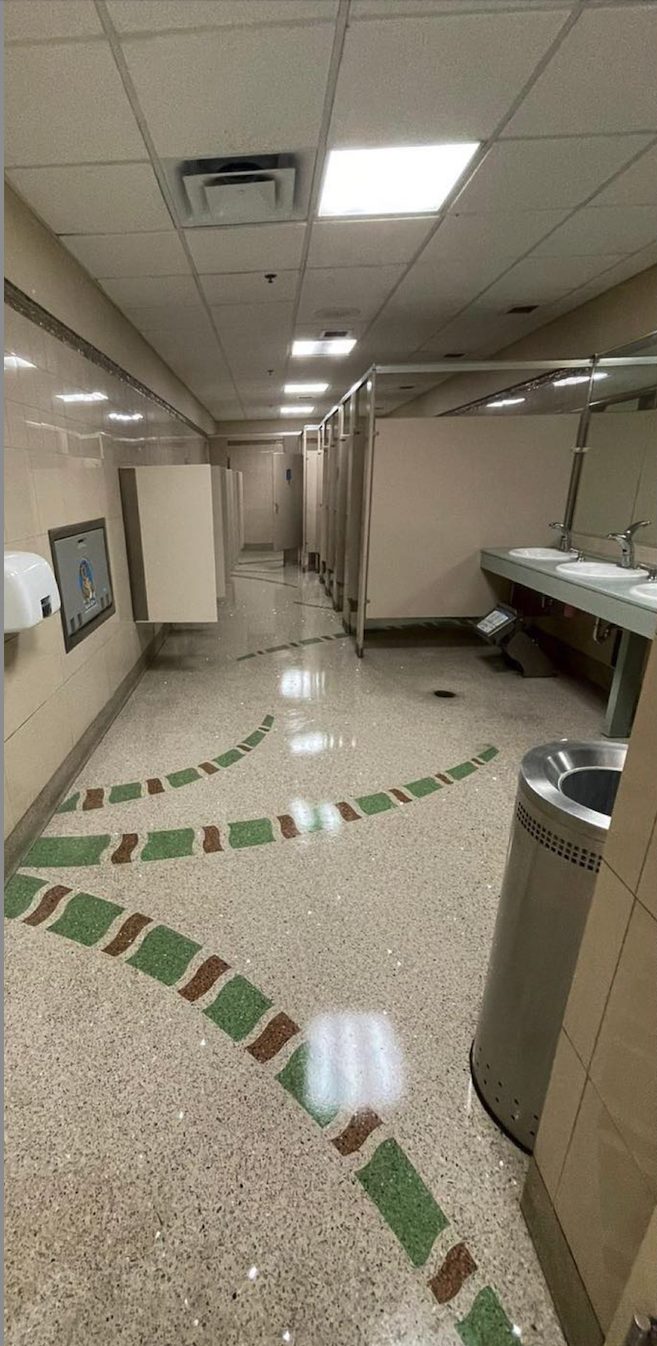 Airport restroom terrazzo dulled by traffic haze with cleaning equipment staged at the sinks
