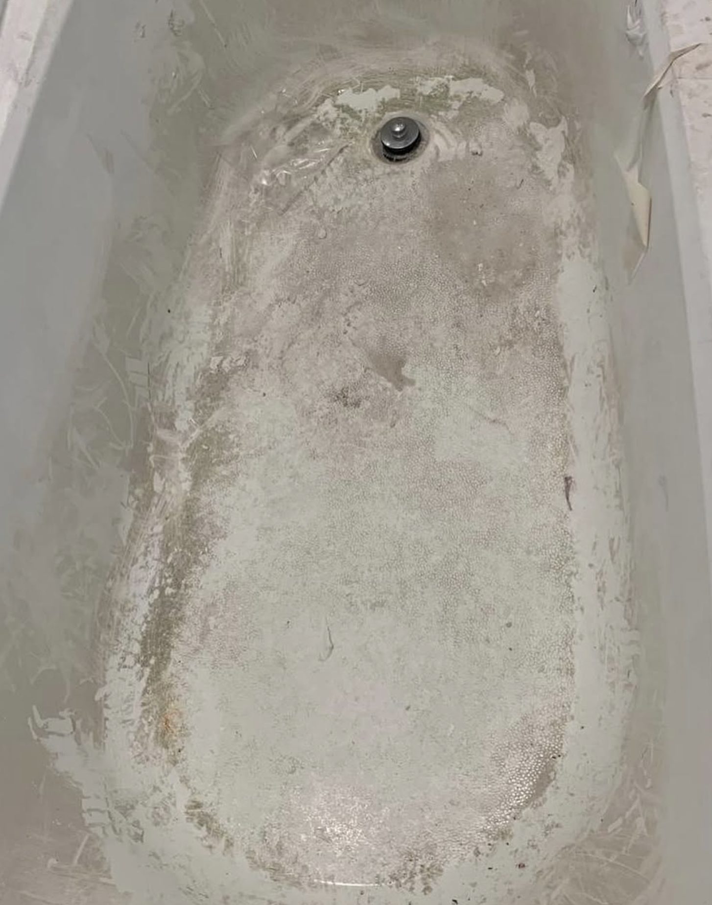Bathtub caked with dried grout haze, plaster splatter and construction dust