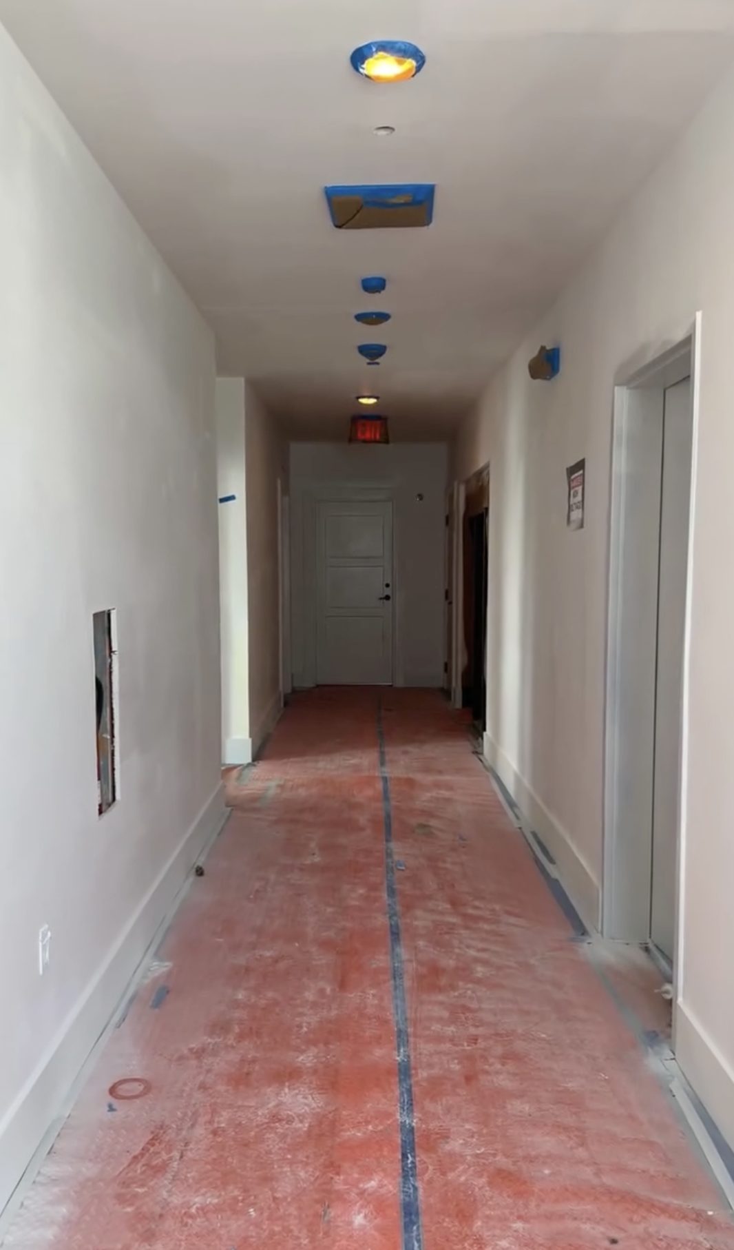 Unfinished corridor on a bare slab with taped ceiling fixtures and construction dust