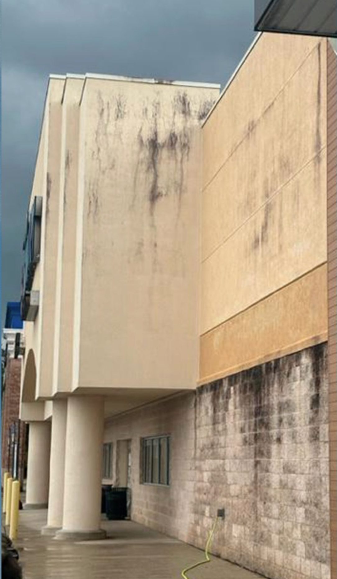 Tan stucco facade streaked with black mold runoff above a grime-darkened block base