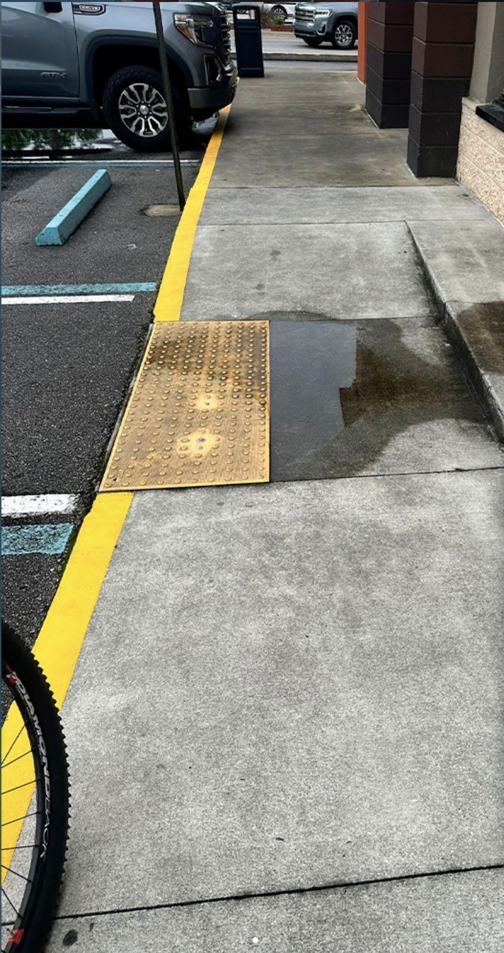 Retail entry sidewalk darkened with grime, its yellow ADA warning pad faded and dull