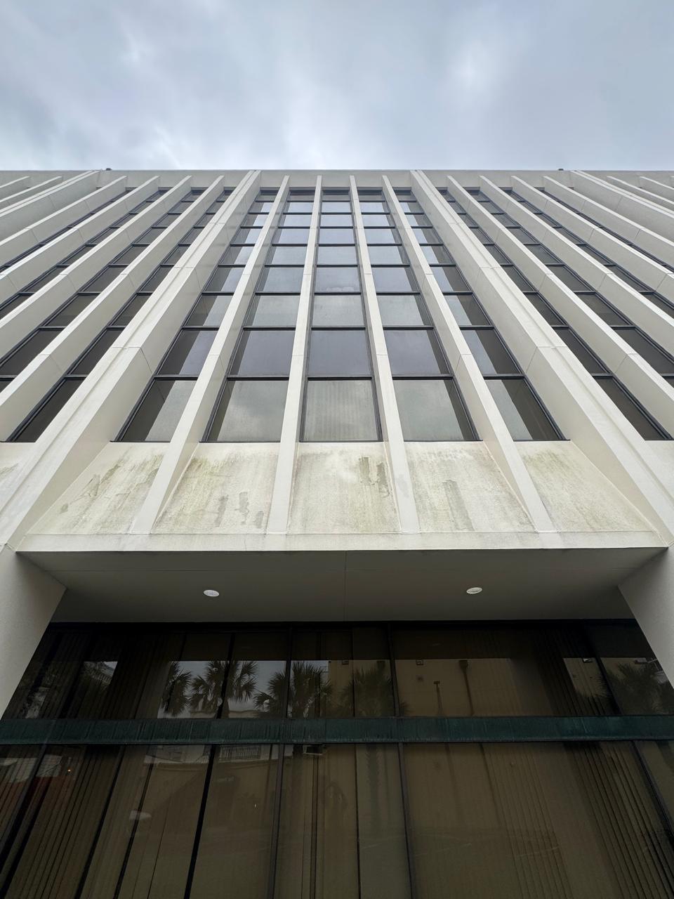 Precast office tower soffit and fins streaked green with algae above the entrance
