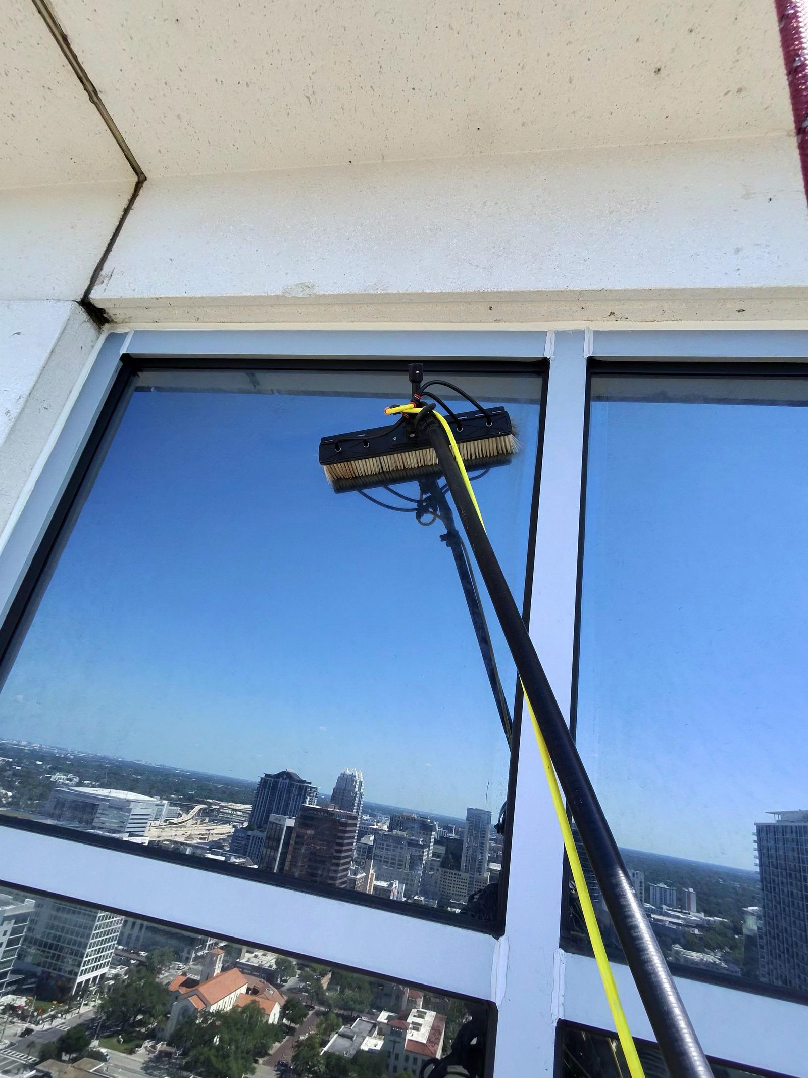 Water-fed pole scrubbing upper-floor courthouse glass above the downtown Orlando skyline