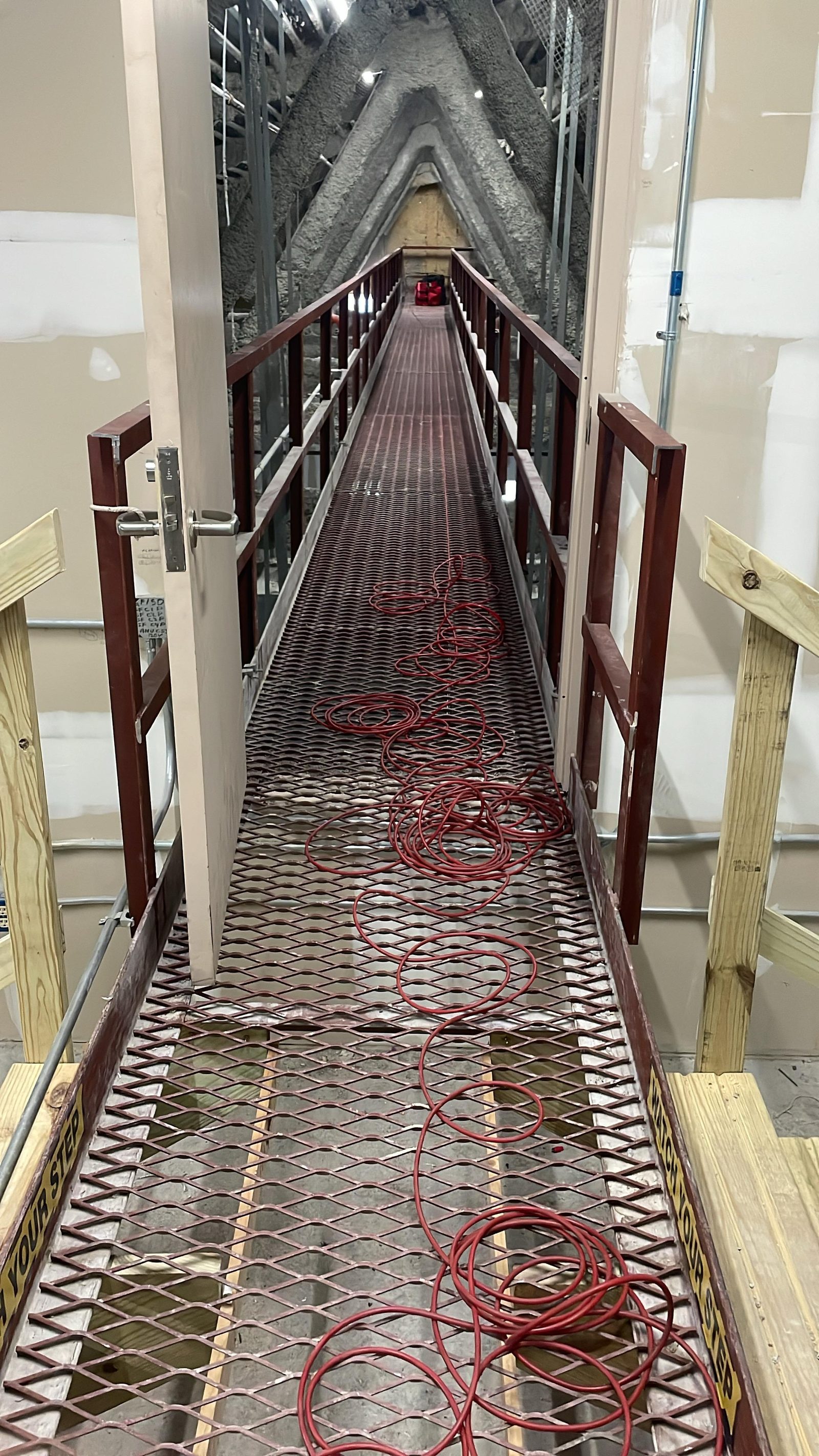 Grated service catwalk with guardrails, watch-your-step markings and a coiled air line